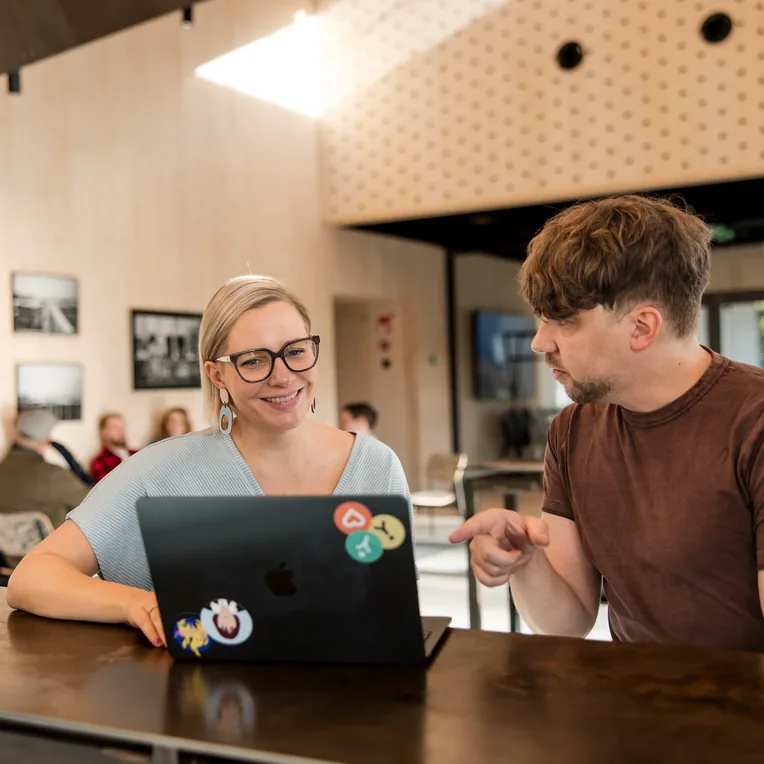 Two colleagues talking over a laptop at a table in a bright, wood-panelled space